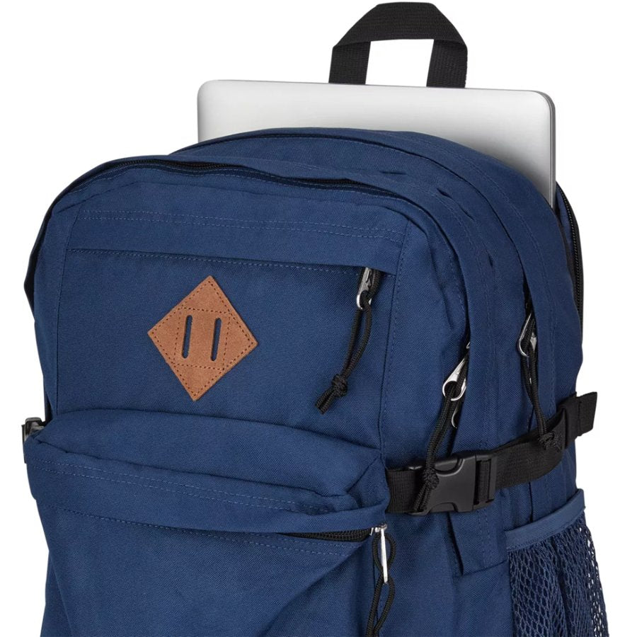 Blue Jansport backpack with a brown patch and black straps, containing a laptop.