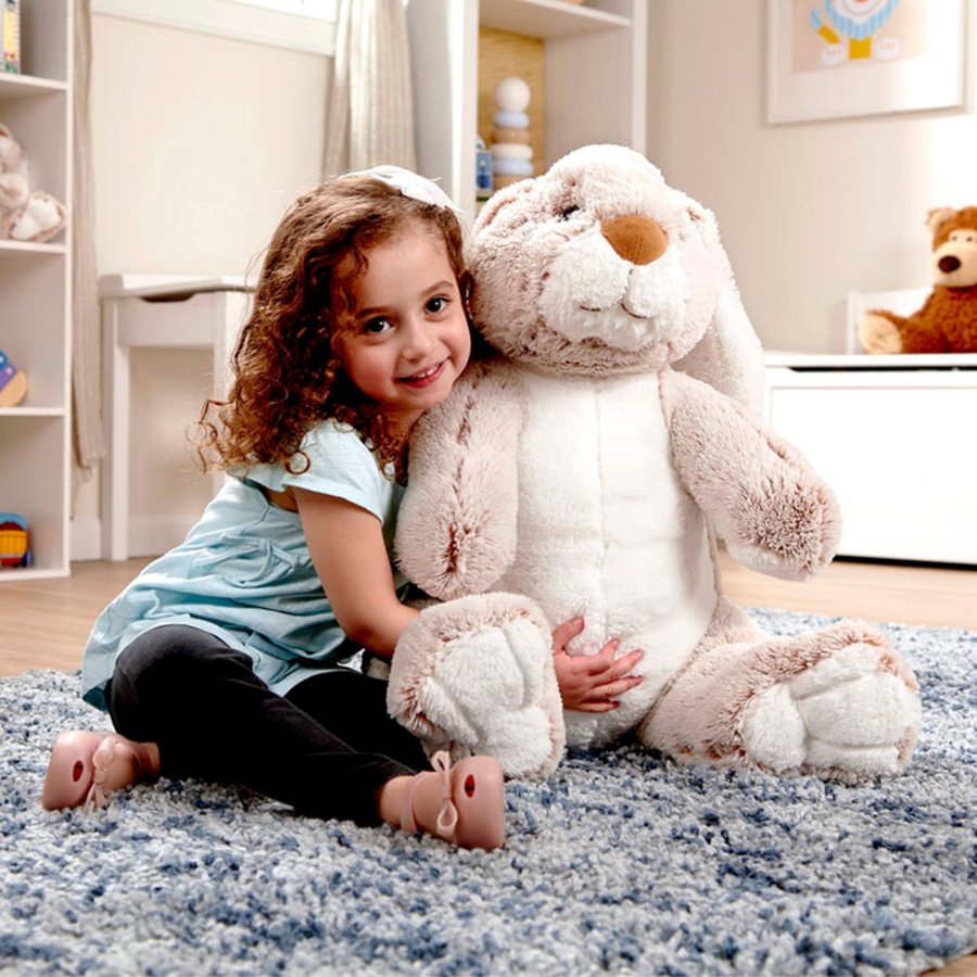 Young girl holding a large plush bunny toy on a carpeted floor.