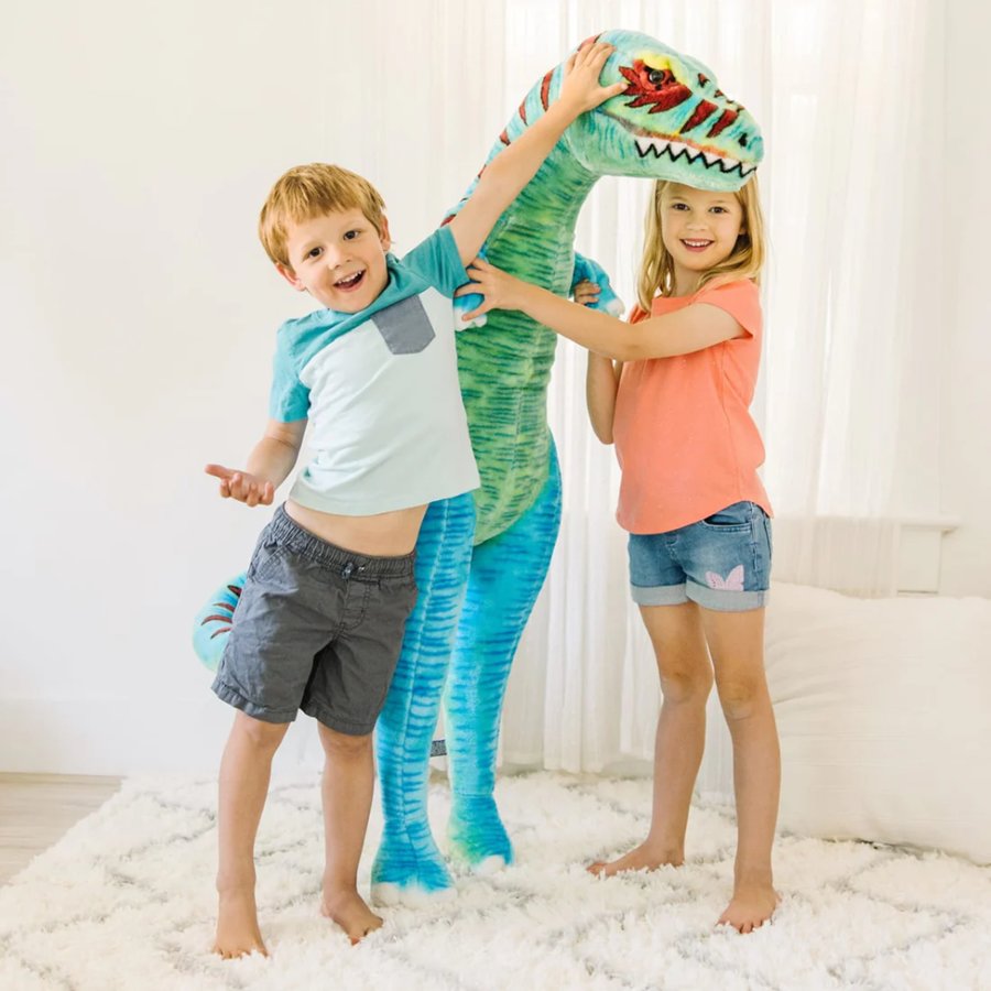 Two children playing with a large inflatable dinosaur toy in a room.