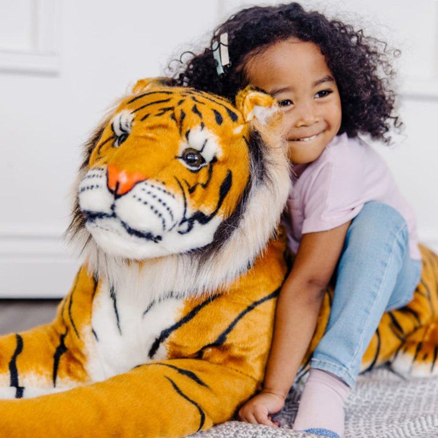 Child sitting next to a large tiger plush toy indoors