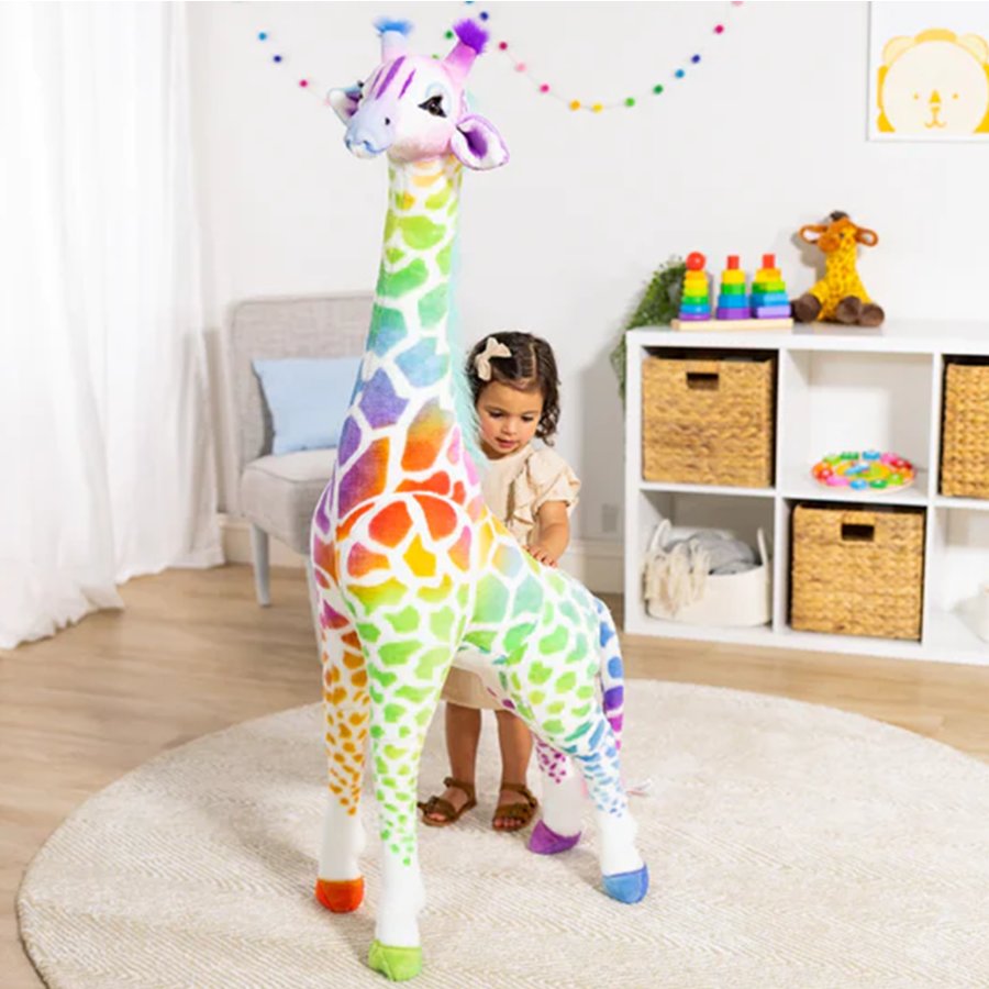 Child playing with a large, colorful stuffed giraffe toy in a room with toys and furniture.