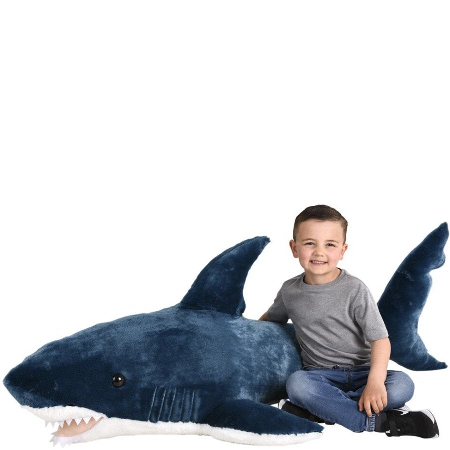 Child sitting next to a large blue shark plush toy on a white background
