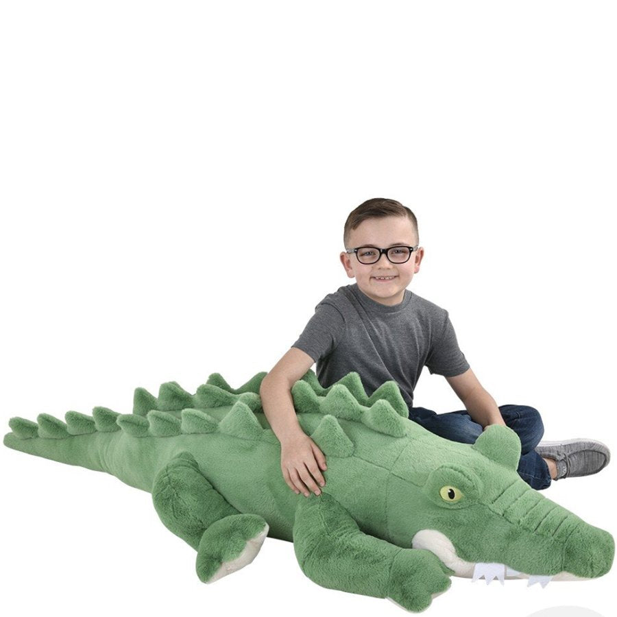 Child sitting with a large green plush alligator toy on a white background