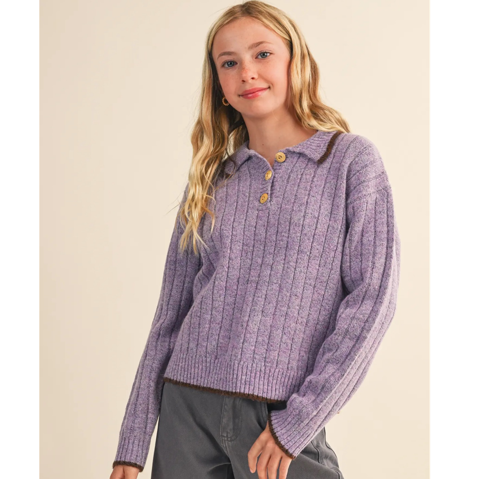 Girl wearing a purple ribbed sweater with button details on a beige background