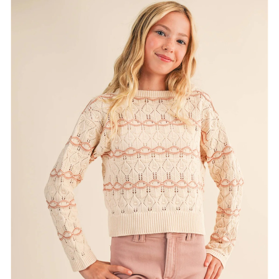 Young girl wearing a beige lace sweater against a plain background