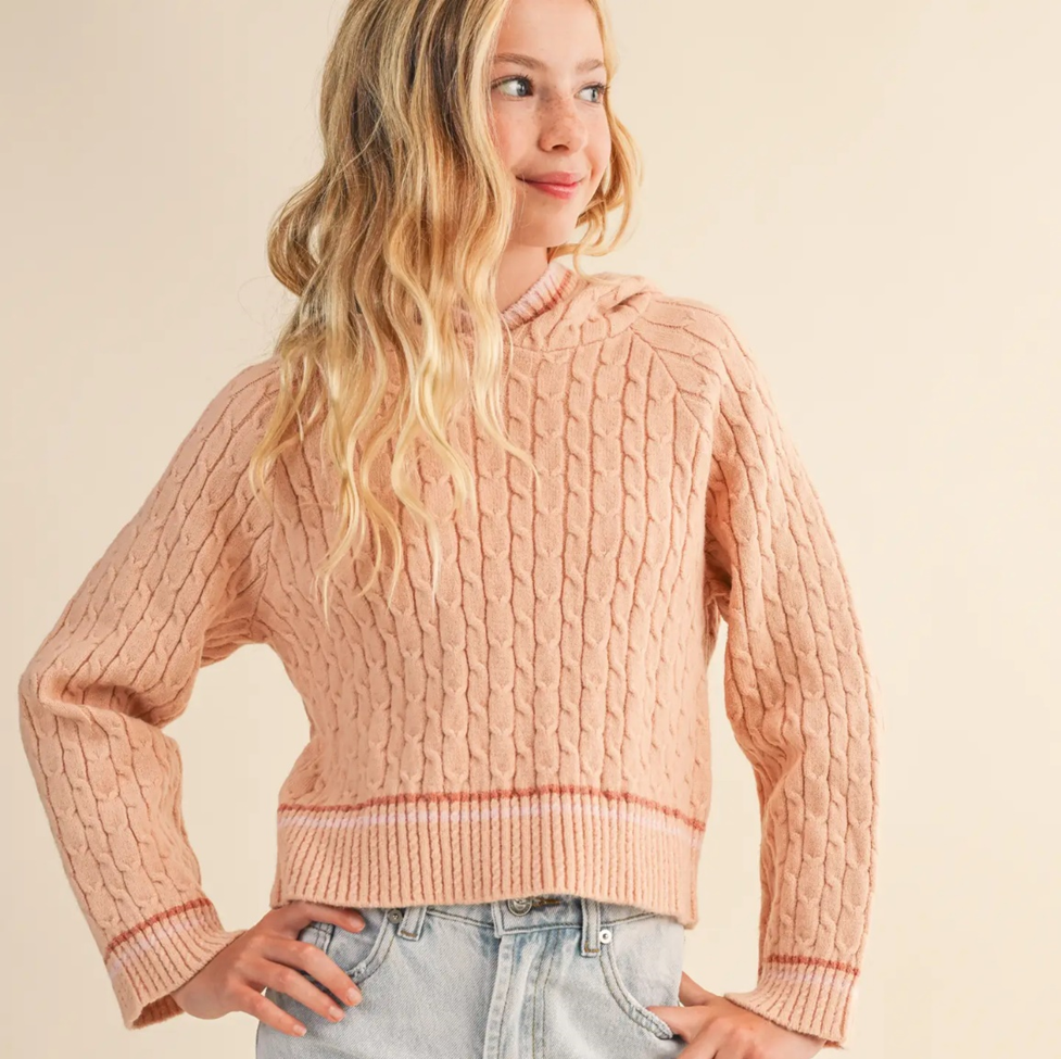 Girl wearing a pink cable knit sweater against a beige background