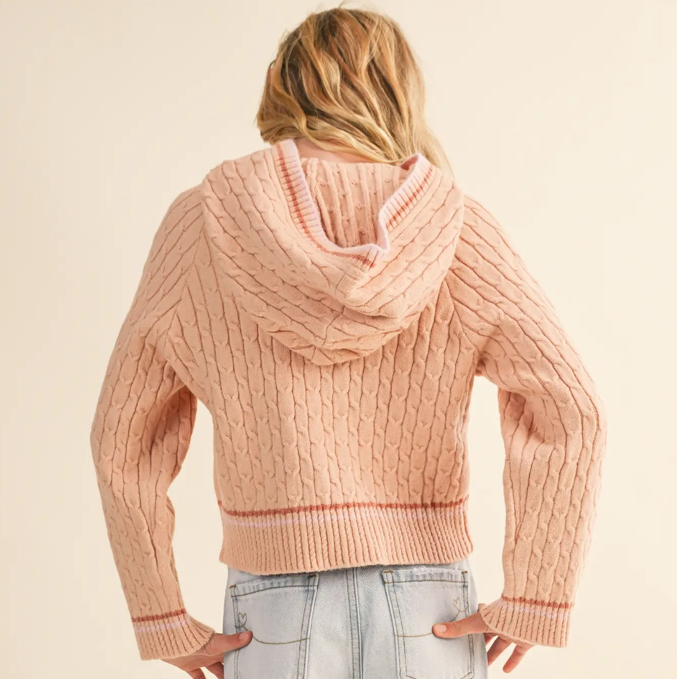 Person wearing a pink cable knit sweater on a beige background