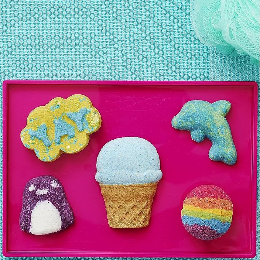 Colorful bath bomb set with cloud, ice cream, dolphin, penguin, and rainbow designs on a pink tray.