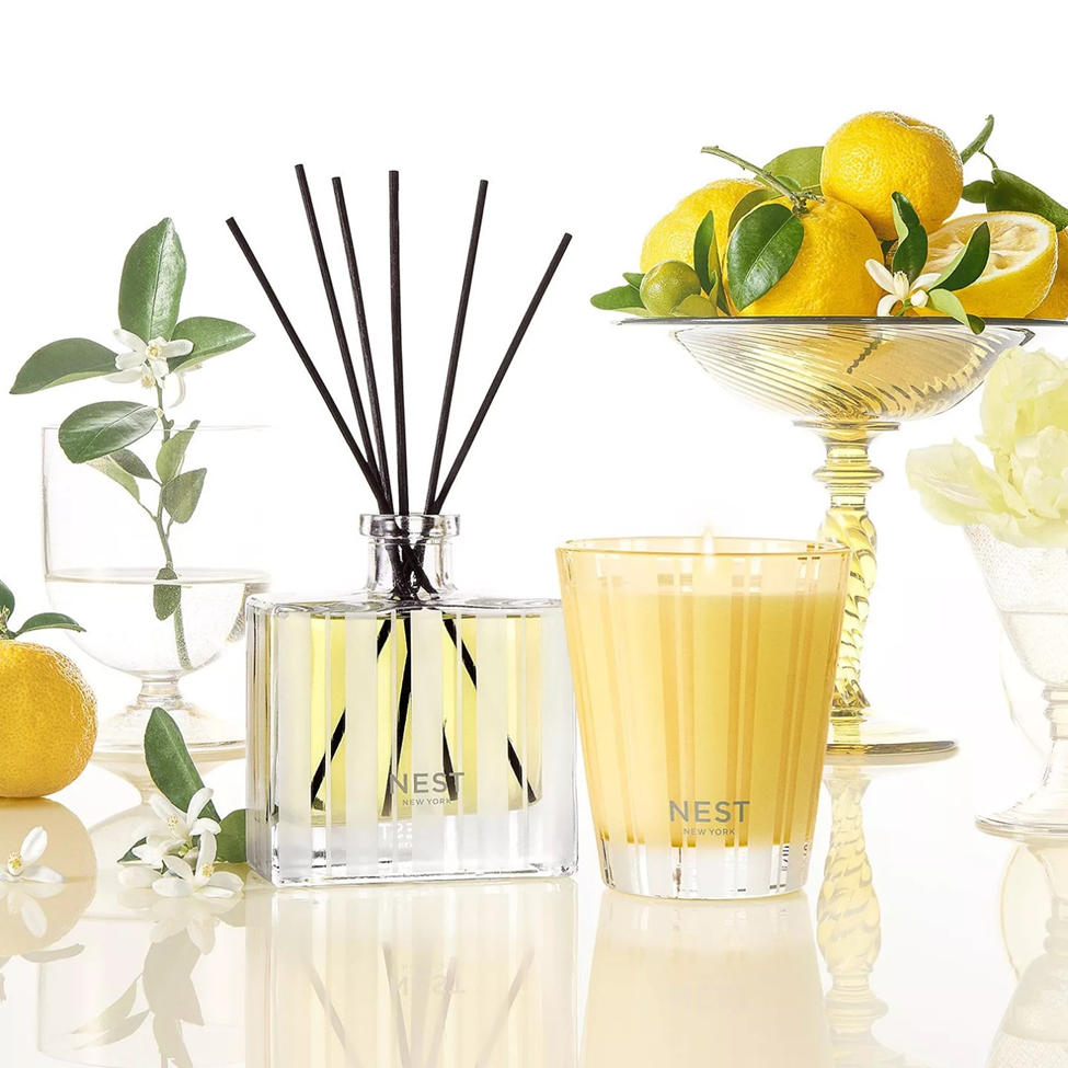 Nest diffuser and candle with lemons and flowers on a reflective surface