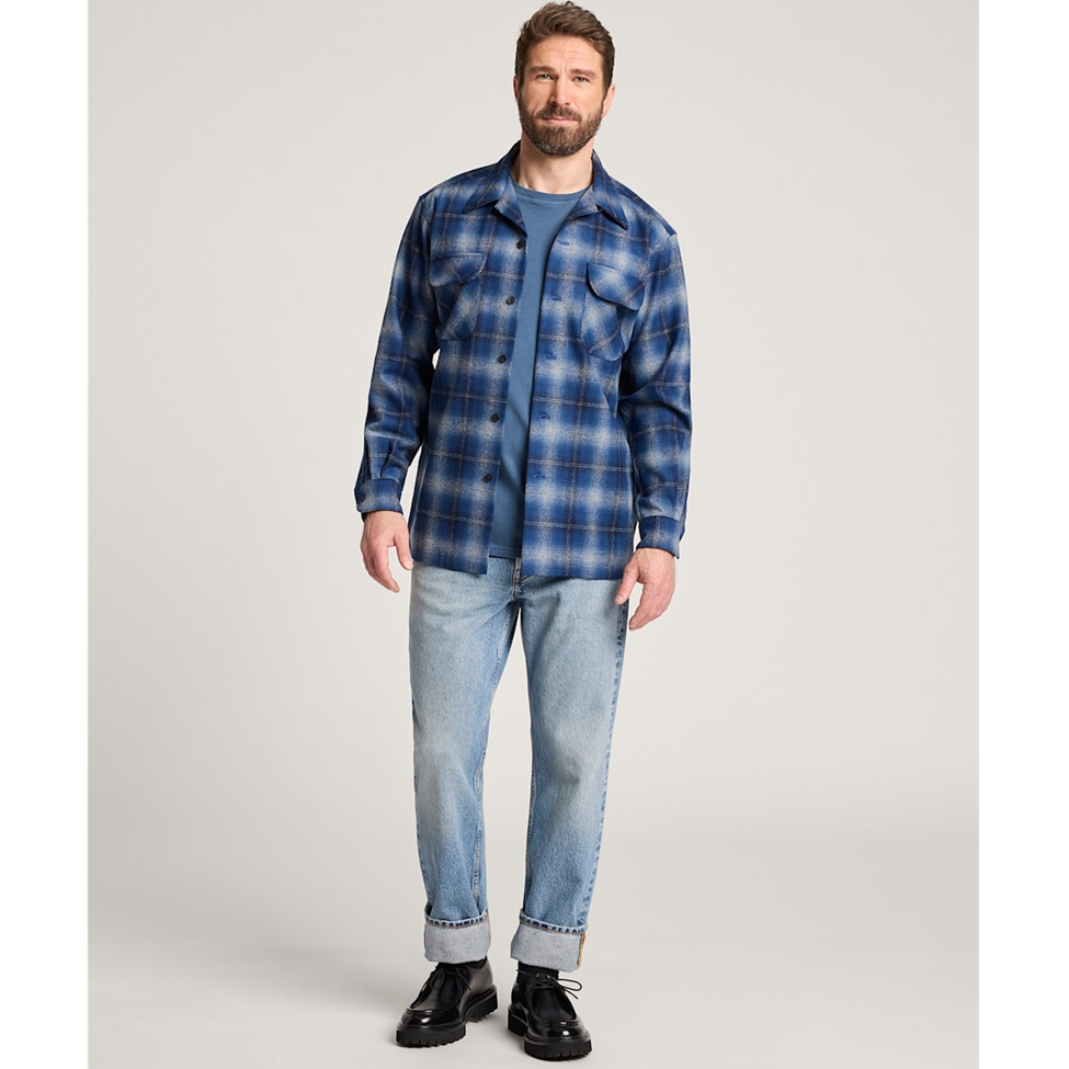 Man wearing a blue plaid shirt and jeans on a light gray background