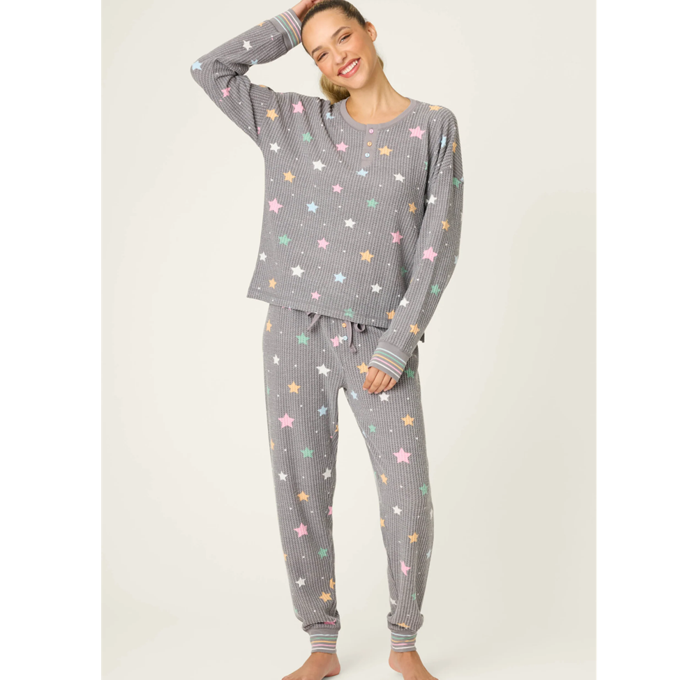 Woman wearing a gray pajama set with colorful star patterns on a white background