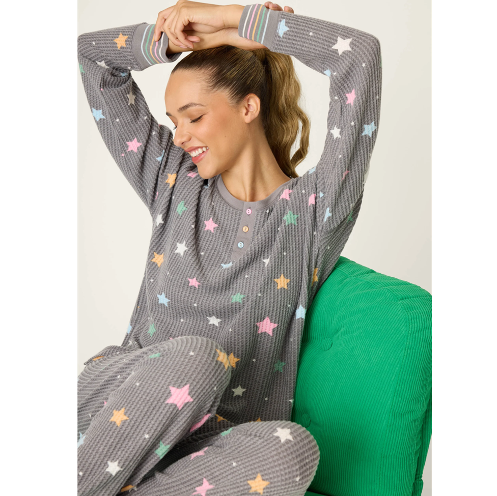 Woman wearing a gray long-sleeve top with colorful star patterns, sitting on a green chair.