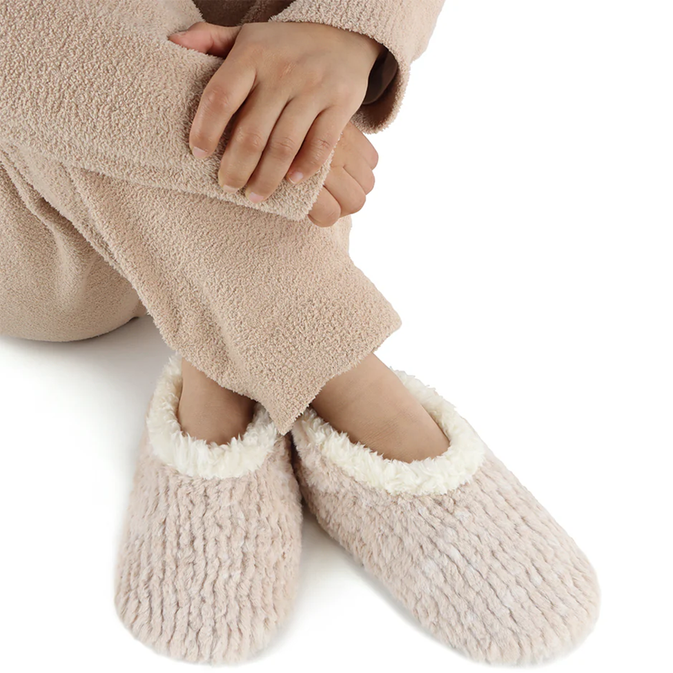 Person wearing beige fuzzy slippers and a matching robe on a white background