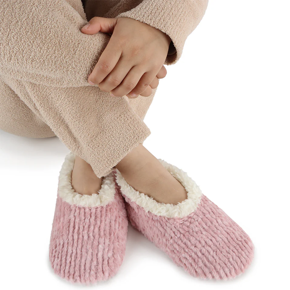Pink slippers with white trim worn by a person in a beige robe on a white background