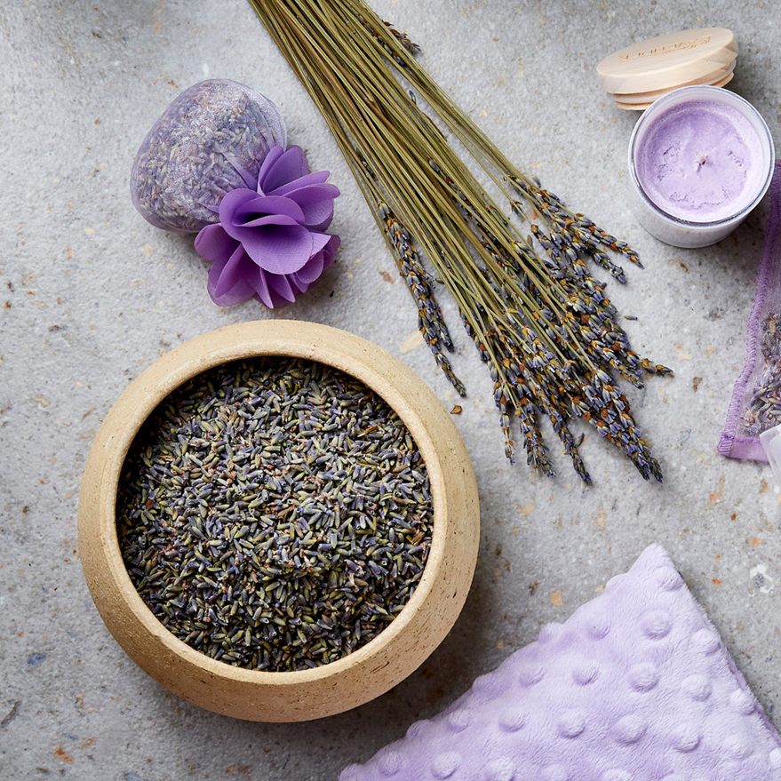 Lavender flowers, bath bombs, and a bowl of lavender petals on a textured surface.