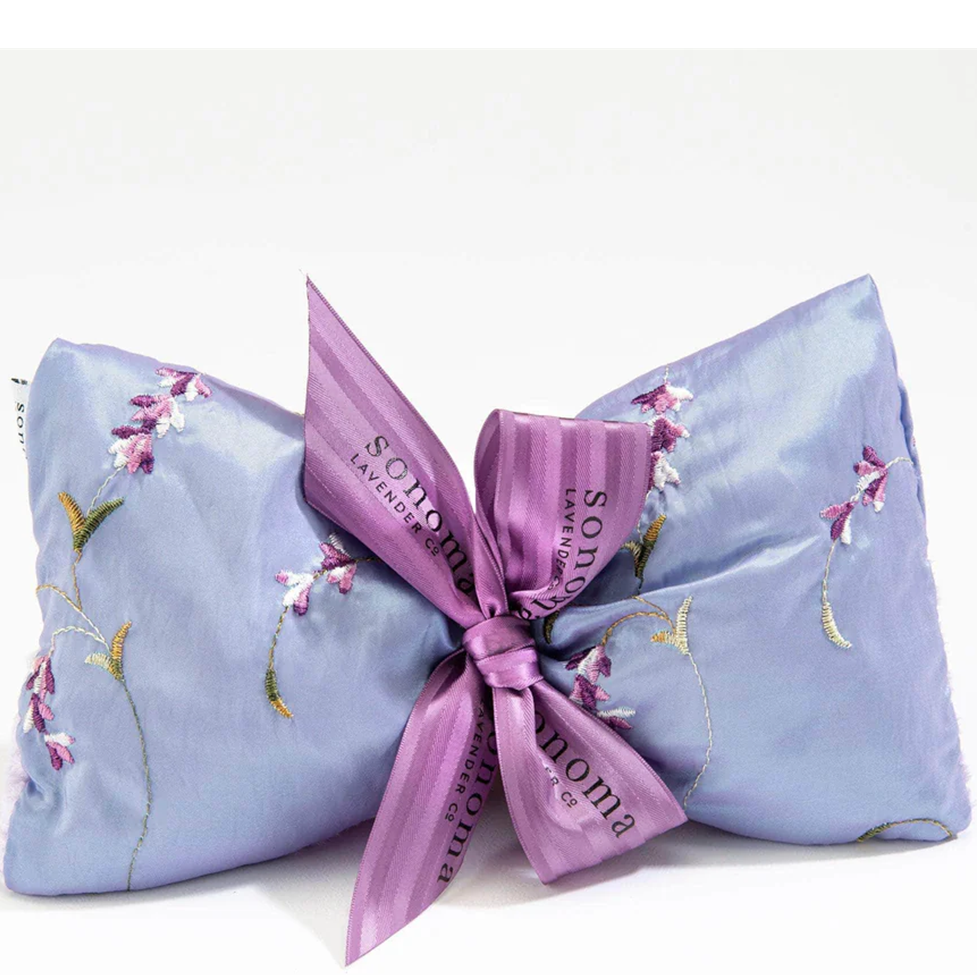 Two lavender pillows with floral embroidery and a pink ribbon on a white background