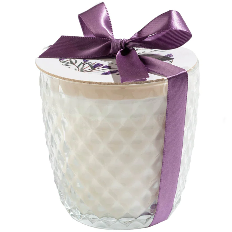 Candle in a glass container with a purple ribbon on a white background