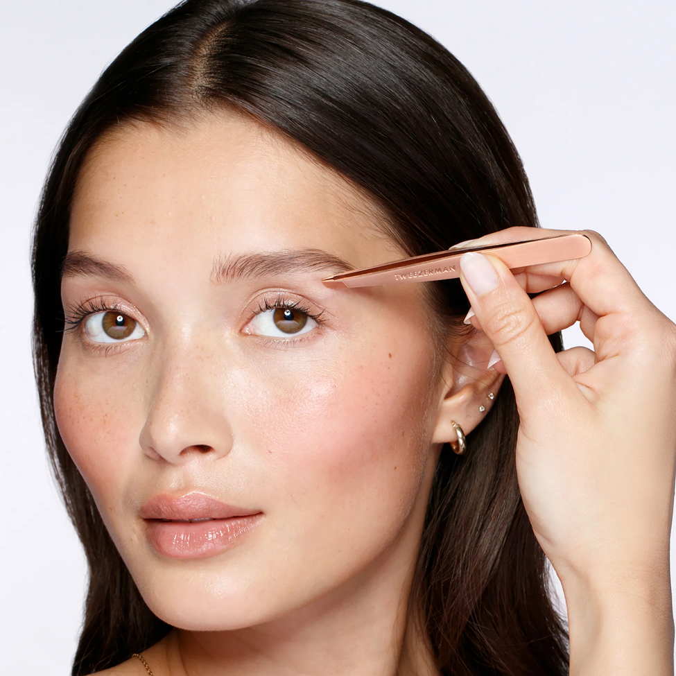 Woman using a brow pencil on her eyebrows with a plain background