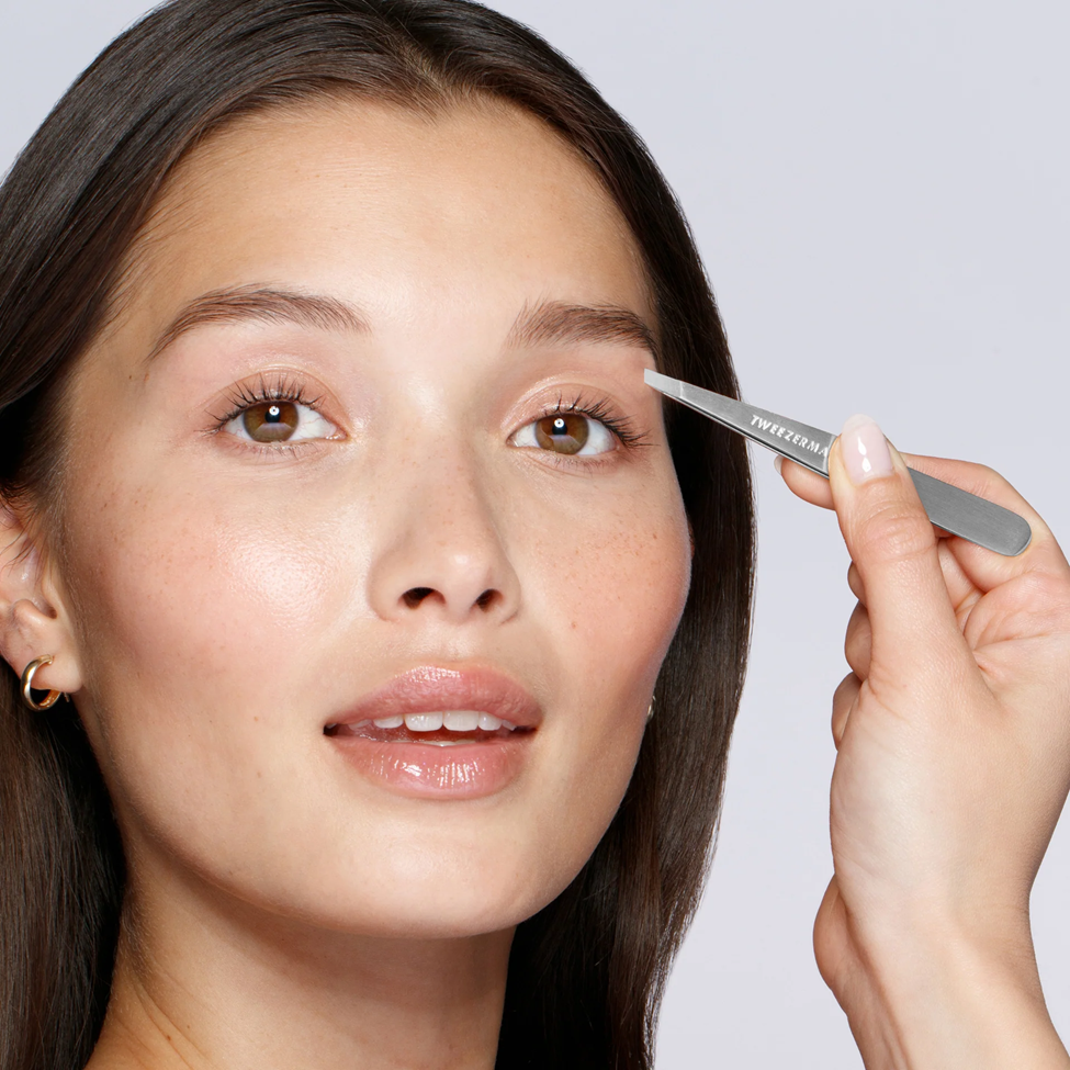 Woman using a brow pencil on her eyebrow with a neutral background