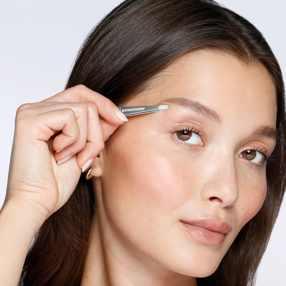 Woman applying eyebrow pencil to her eyebrows with a neutral background