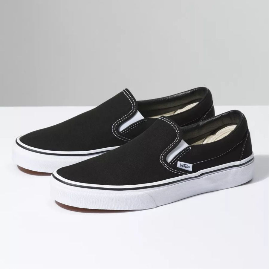 Black slip-on sneakers with white soles on a light gray background