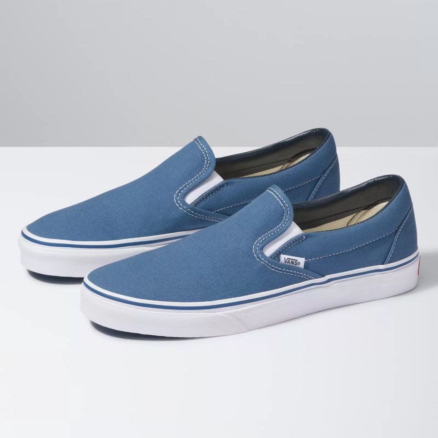 Pair of blue slip-on sneakers with white soles on a light gray background