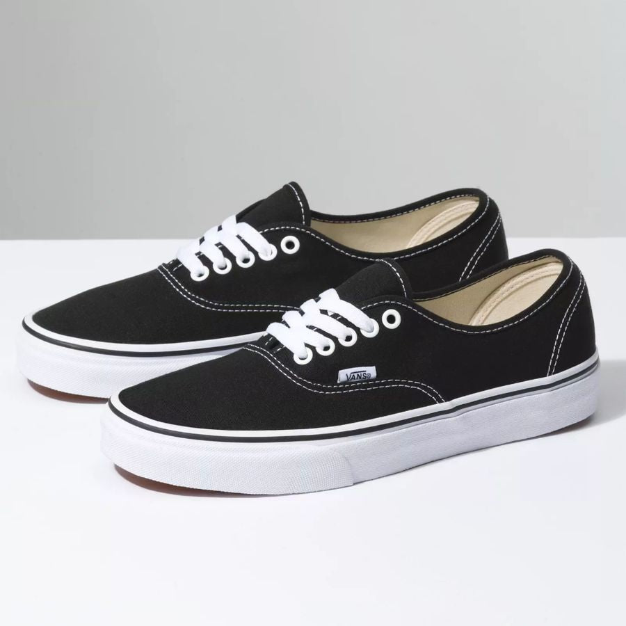 Pair of black sneakers with white laces on a light gray background