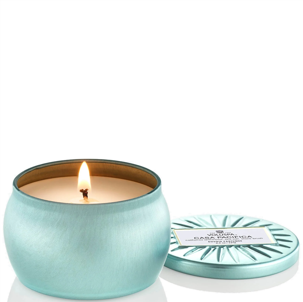 Lighted teal candle in a tin with a matching lid on a white background