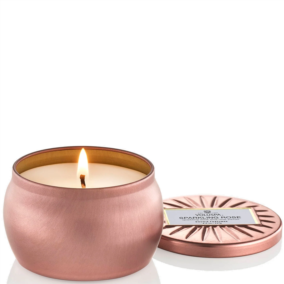 Copper candle with a lit wick and matching lid on a white background