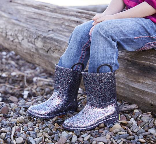 Person wearing sparkly purple rain boots sitting on a log outdoors.