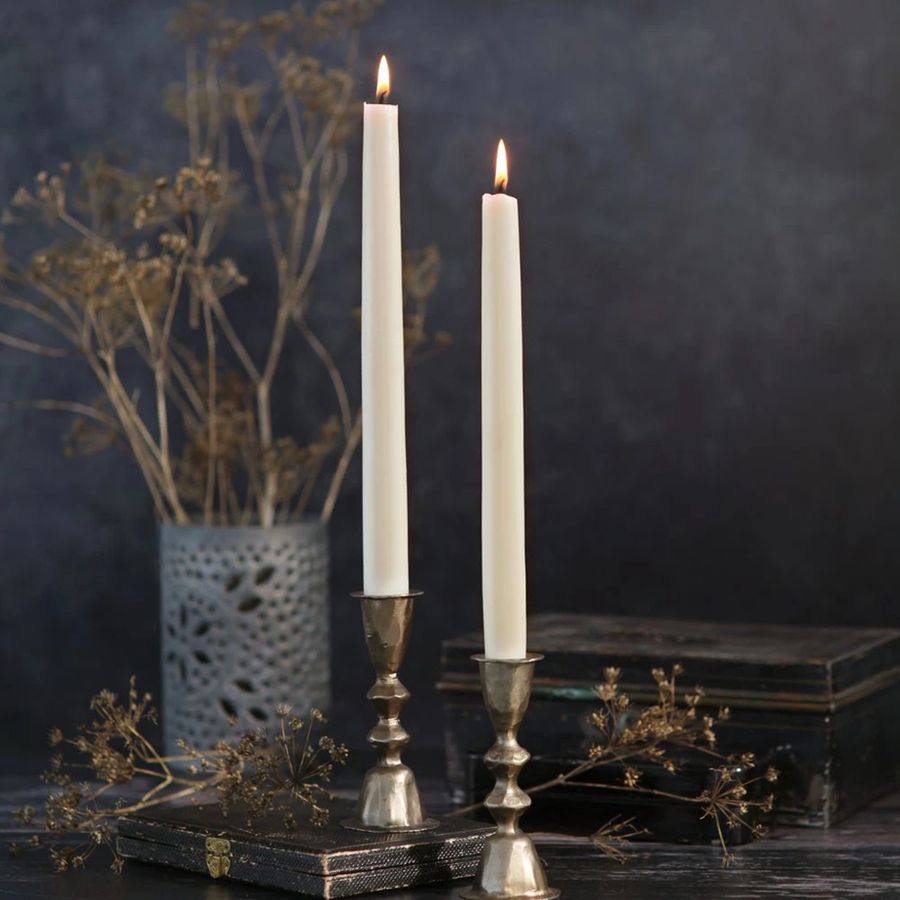 Two lit candles in silver holders with dried flowers and books on a dark background