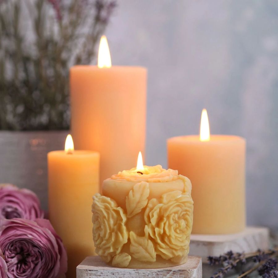 Three candles, one with floral design, surrounded by flowers and lavender on a soft focus background.