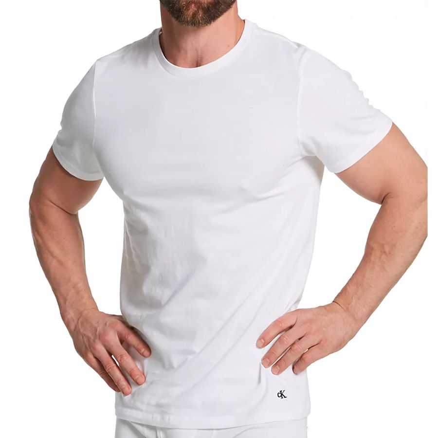 A man wearing a white short-sleeve crewneck t-shirt with a small black Calvin Klein logo on the bottom right hem, shown against a plain white background.