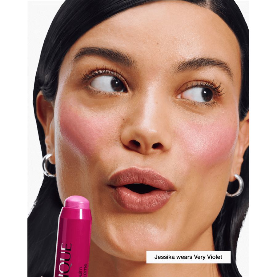Woman with pink makeup and a pink lip balm labeled 'Very Violet' on a white background