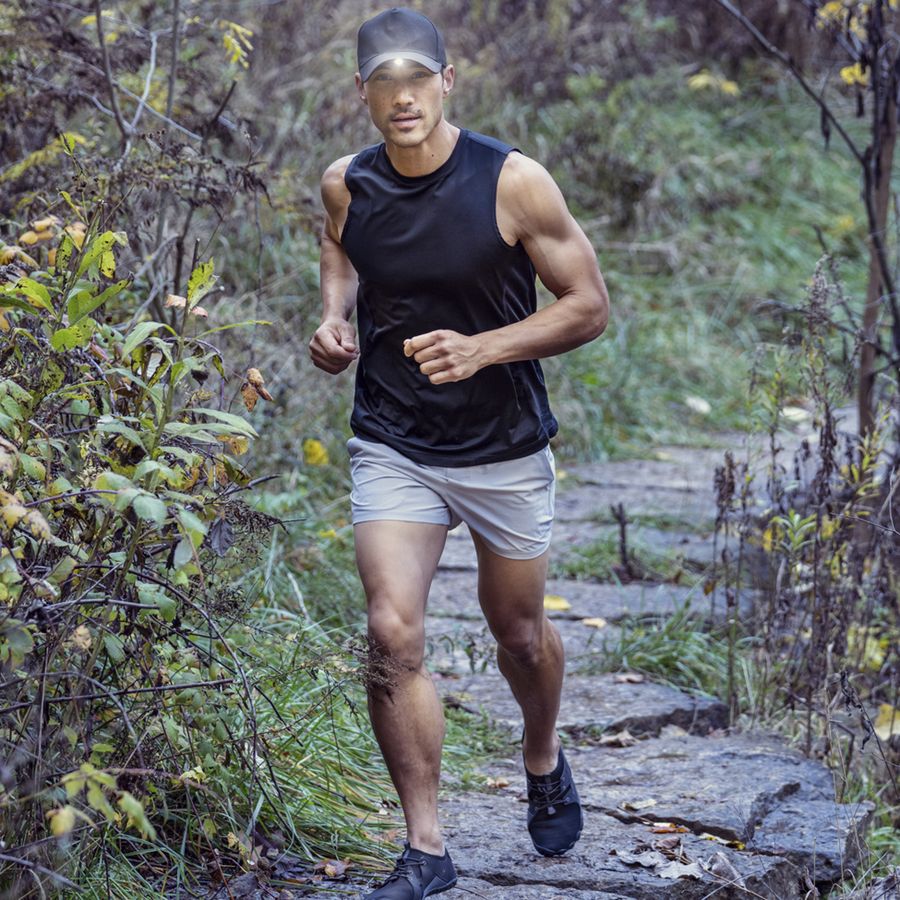 Man running on a forest path wearing a black tank top and shorts.