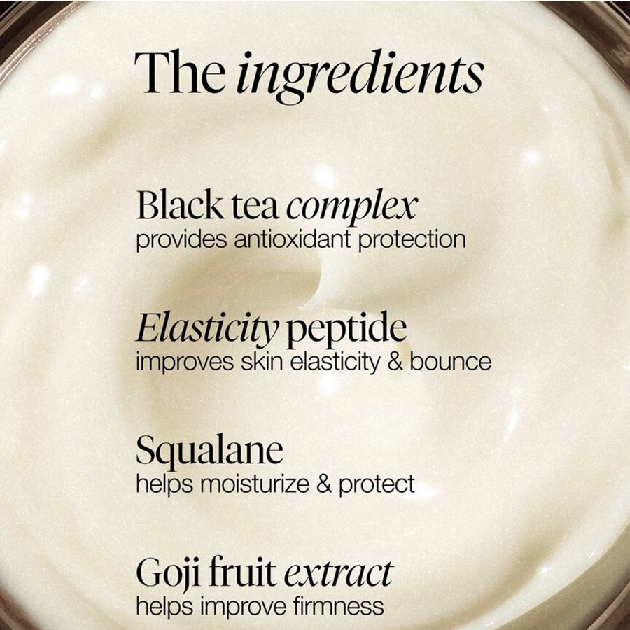 Close-up of a cream-colored cosmetic jar with text overlay detailing ingredients: black tea complex, elasticity peptide, squalane, and goji fruit extract.
