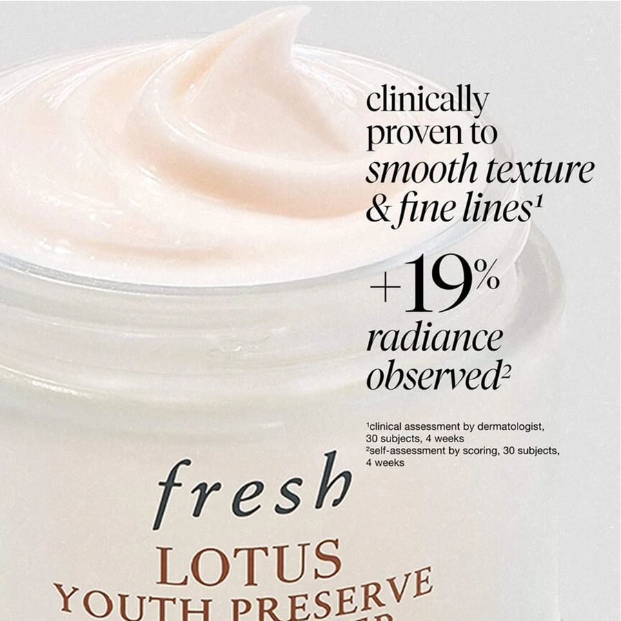 Close-up of a white cosmetic jar filled with pale pink cream, with printed text reading 'fresh LOTUS YOUTH PRESERVE' and marketing copy about smooth texture and fine lines.