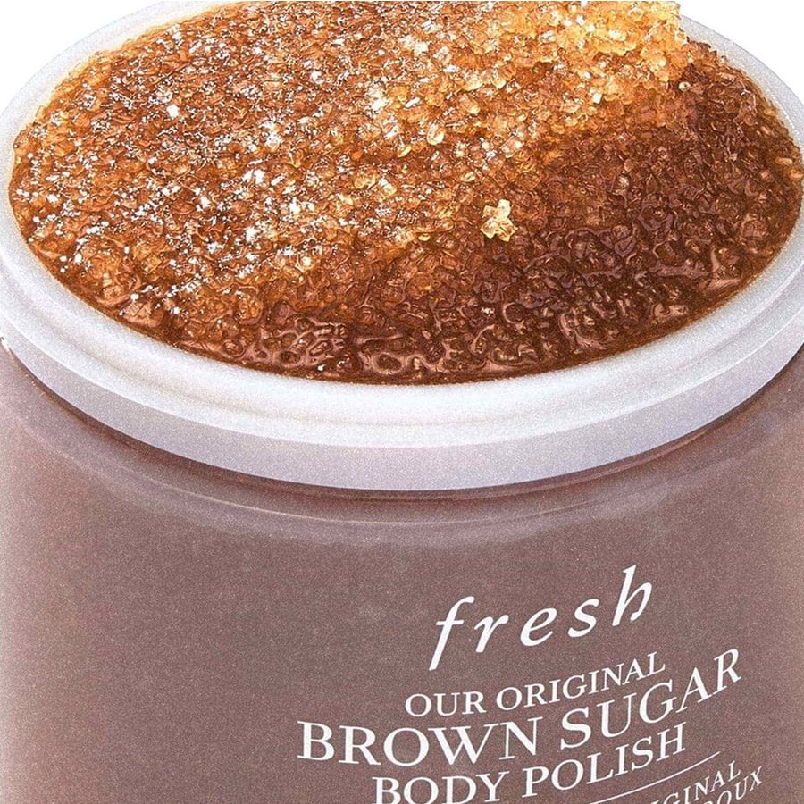 Close-up of a jar of Fresh Our Original Brown Sugar Body Polish, showing the white lid open to reveal a thick, granular brown sugar scrub inside. The jar is a warm taupe-brown color with white text.