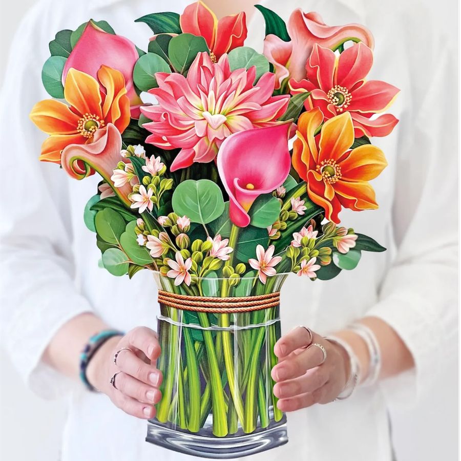 Colorful bouquet of flowers in a clear vase held by a person wearing a white shirt.