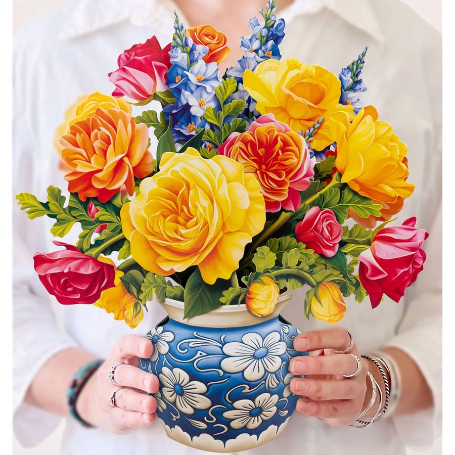 Colorful bouquet of flowers in a decorative blue and white vase held by a person.
