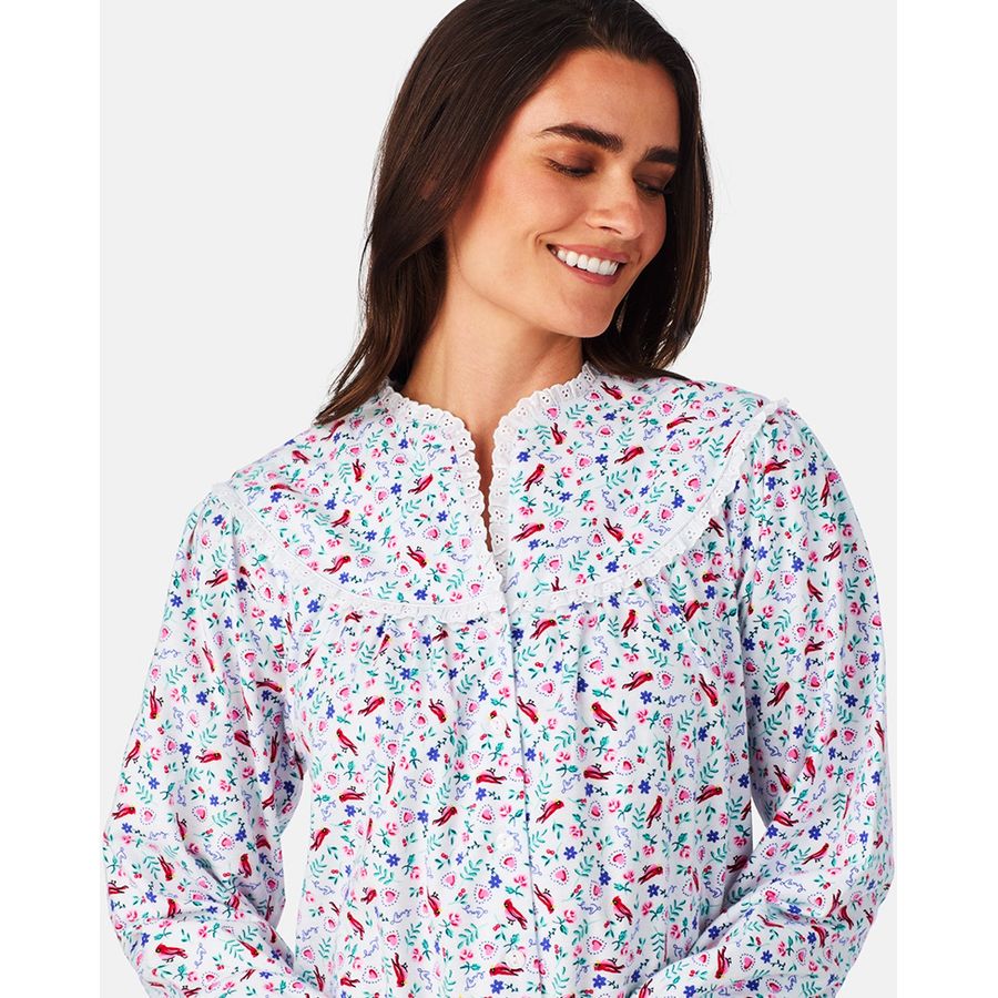 Woman in floral print nightgown with lace collar, smiling softly. Features long sleeves and a mix of pink, red, blue, and green flowers.