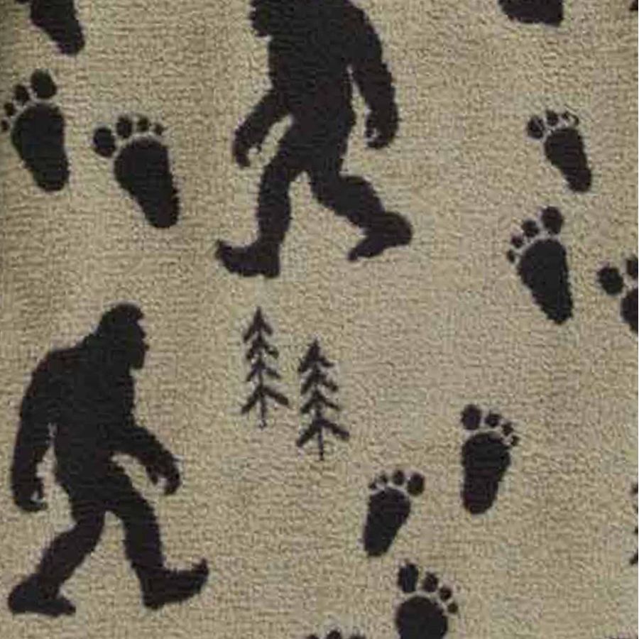 A close-up of a beige textured surface with a repeating black pattern of bigfoot silhouettes, bear paw prints, and small pine trees.