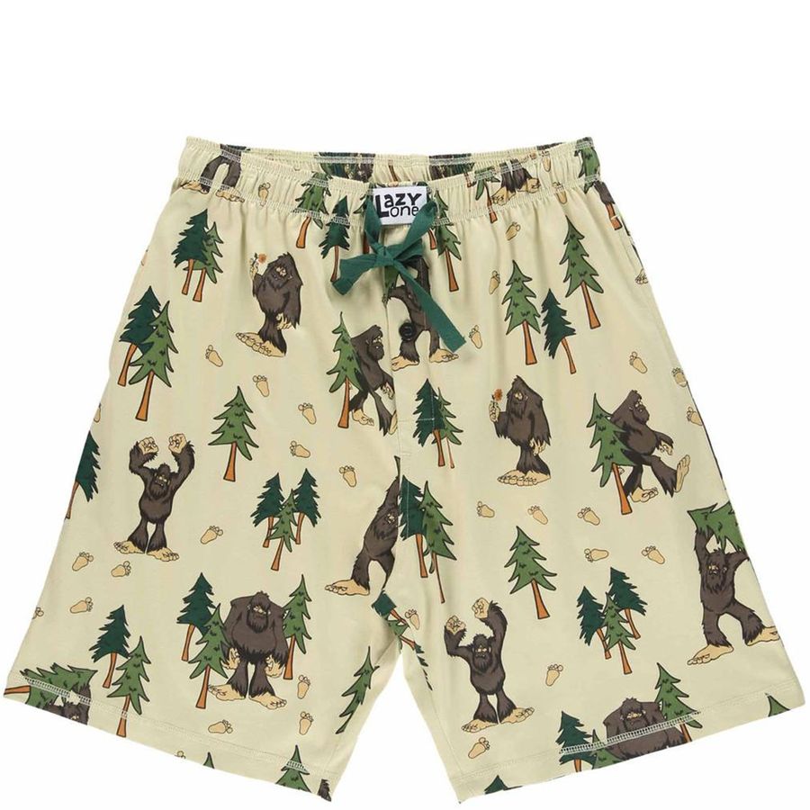 A pair of men's shorts featuring an all-over print of Bigfoot figures, pine trees, and acorns on a light beige background, with a dark green drawstring bow at the elastic waistband.